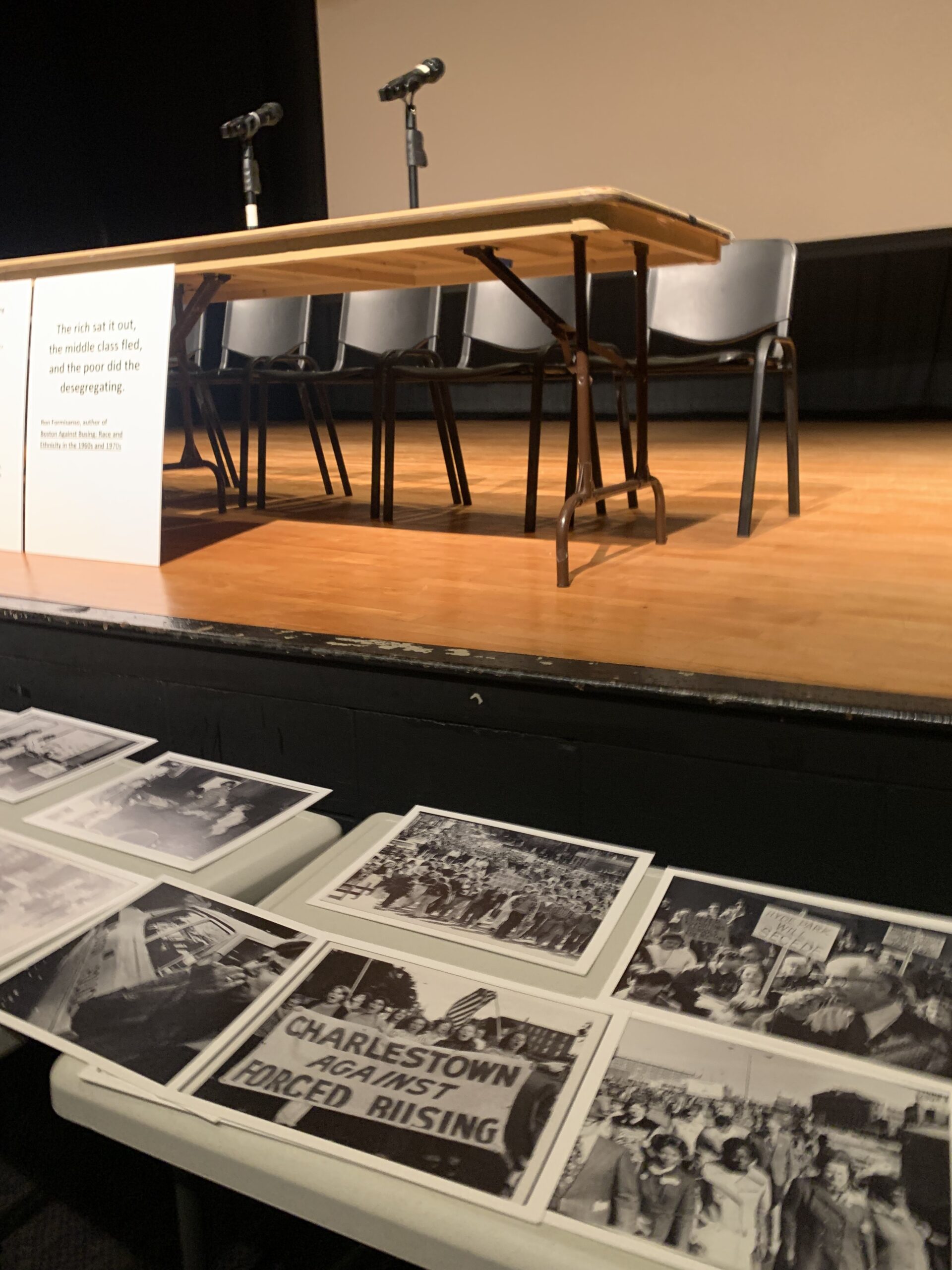 A table covered with archival images and documents in front of a stage set for a forum